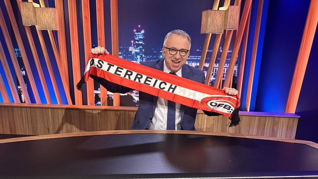 © ORF/Gebhardt Productions Peter Klien im "Gute Nacht Österreich"-Studio hält einen rot-weißen ÖFB-Schal mit der Aufschrift „Österreich“ hoch.