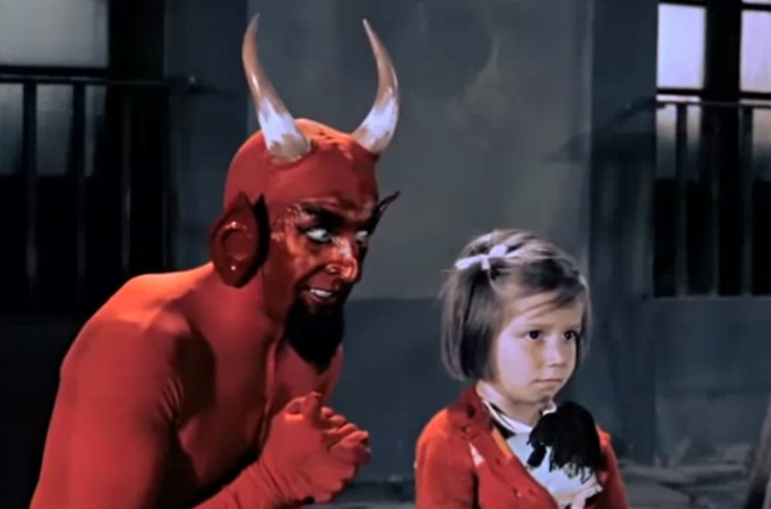 A guy in a devil costume talking to a little kid