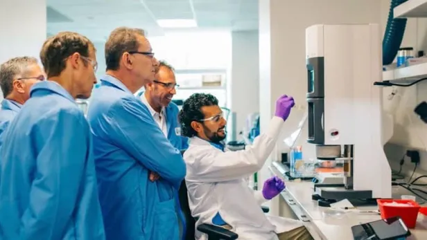 Photograph of scientists in lab coats watching a colleague examine a sample thumbnail