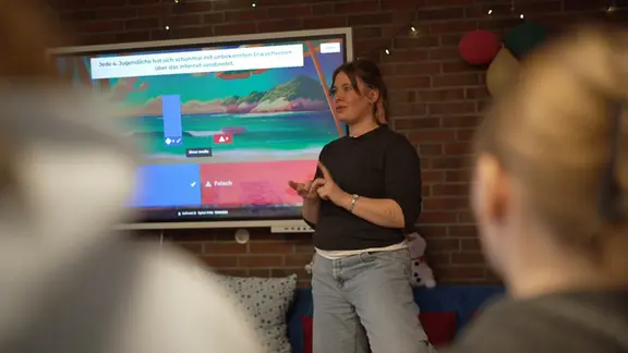Frau steht vor einer Leinwand und spricht zu jungen Zuhörenden