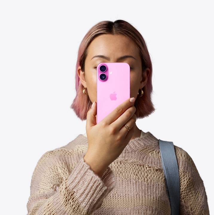 امراة تحمل iPhone16 باللون الوردي أمام وجهها ويظهر الجزء الخلفي الخارجي، ونظام الكاميرا المزدوجة في الزاوية العلوية اليسرى.